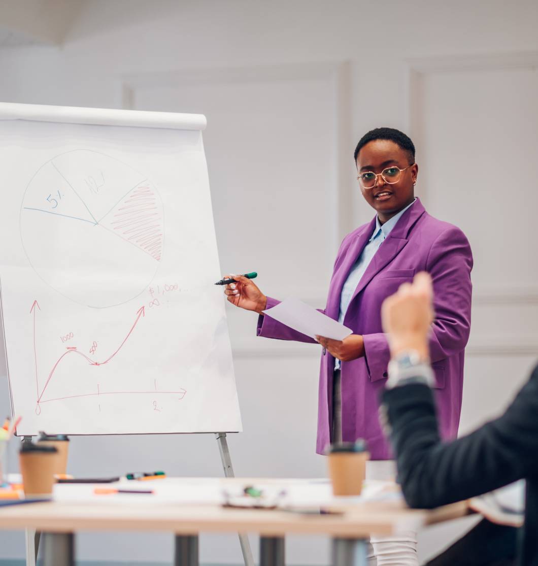 African american woman presenting research to team and explaining sales reports while pointing at charts on white board. Black woman boss standing at flipchart and explaining new strategy of company.
